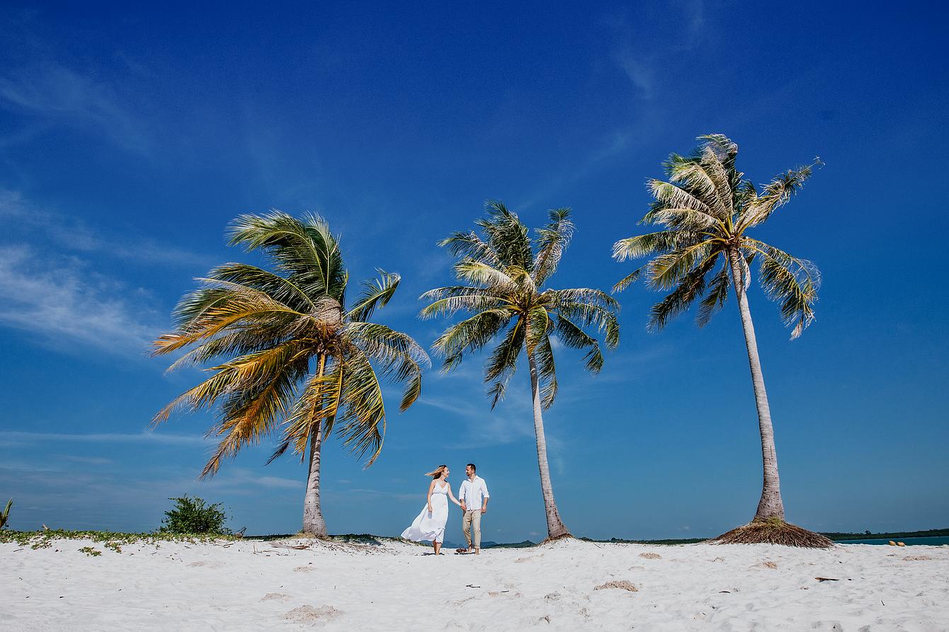 Eleopment Heiraten in Thailand Brautpaar steht am weißen Sandstrand zwischen zwei Kokospalmen