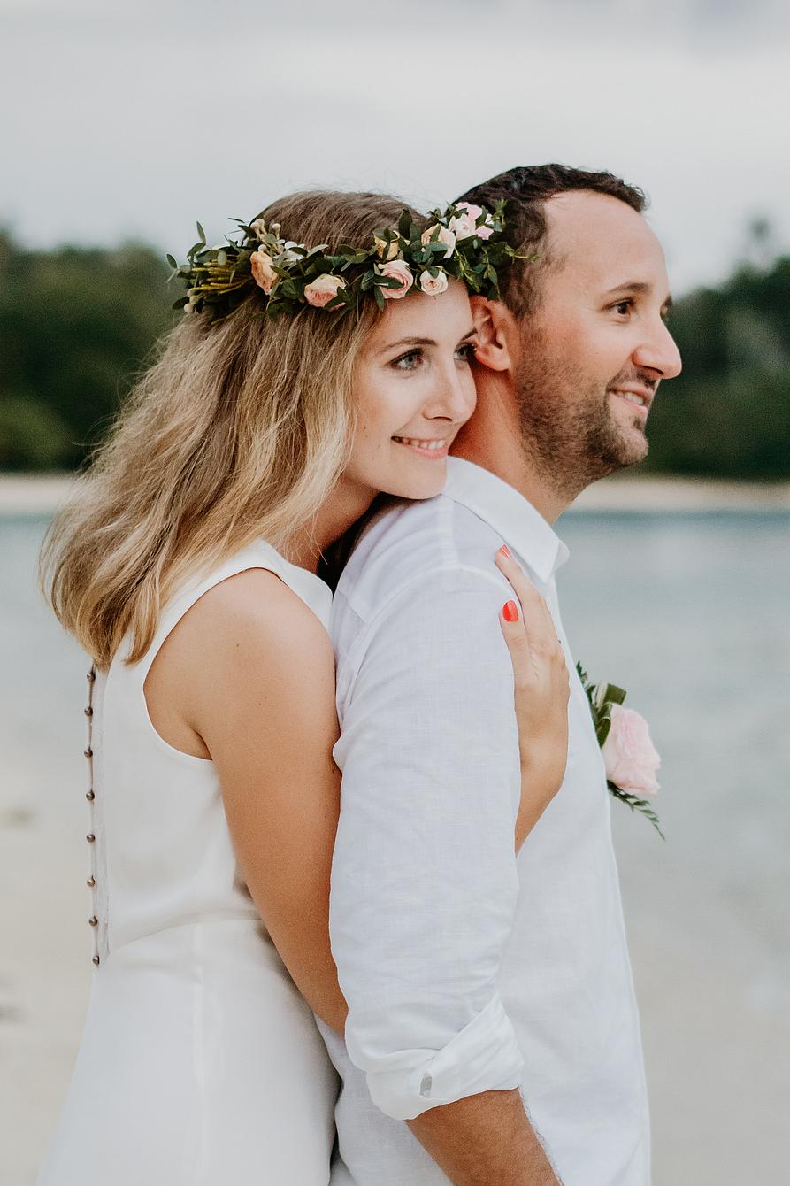 Elopement Hochzeit. Am Strand umarmt die Braut den Bräutigam von hinten