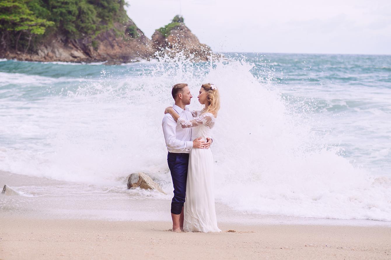 Brautpaar steht am Strand mit Wellen und Gischt im Hinterund