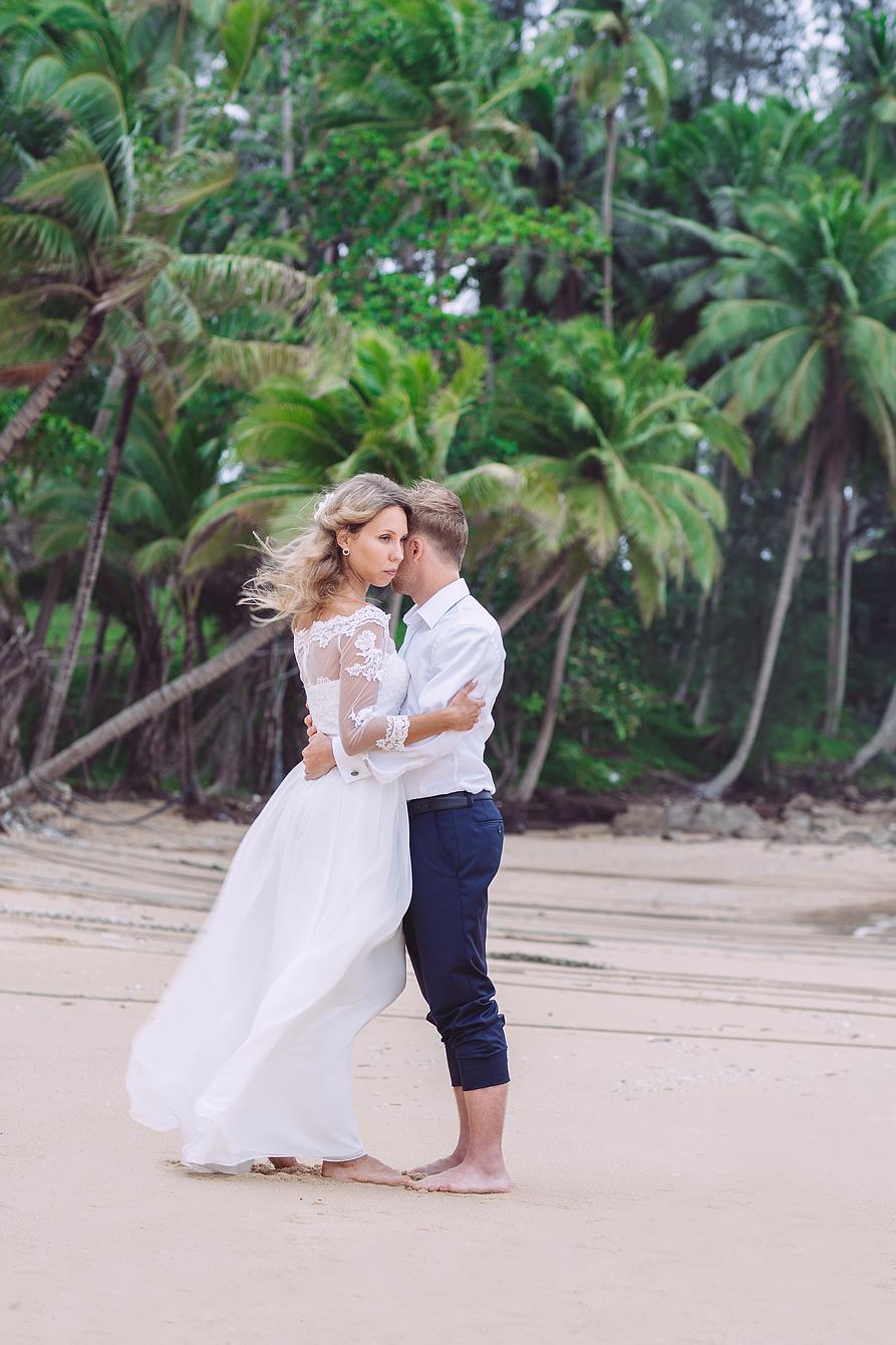 Brautpaar umschlungen am Strand von Phuket mit Kokospalmen im Hintergrund