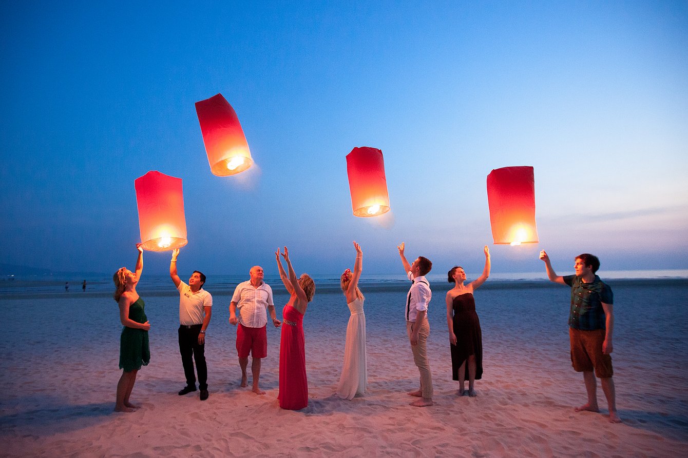A group of wedding guests releases sky lanterns on a beach in Thailand