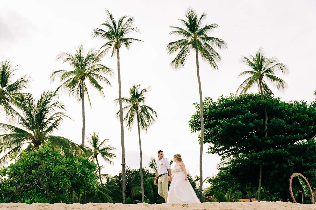 Bride and groom walking hand in hand on a palm-fringed beach at New Star Beach Resort, Koh Samui.