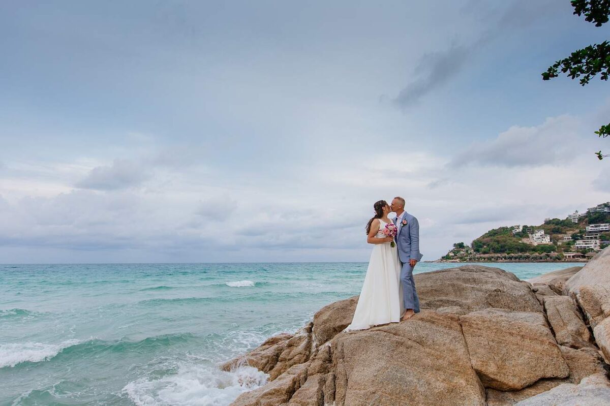 Bride and groom standing on rocks by the sea at New Star Beach Resort, Koh Samui.
