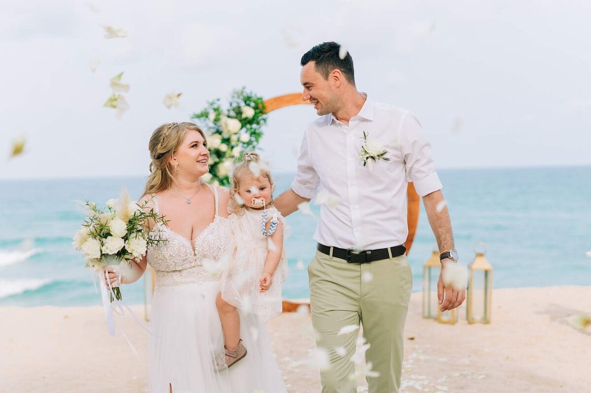 Bride and groom walking on the beach with their young daughter after the ceremony at New Star Beach Resort, Koh Samui.