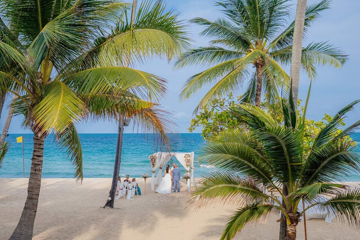 Wedding ceremony on the beach at New Star Beach Resort, Koh Samui, framed by palm trees and overlooking the turquoise sea.
