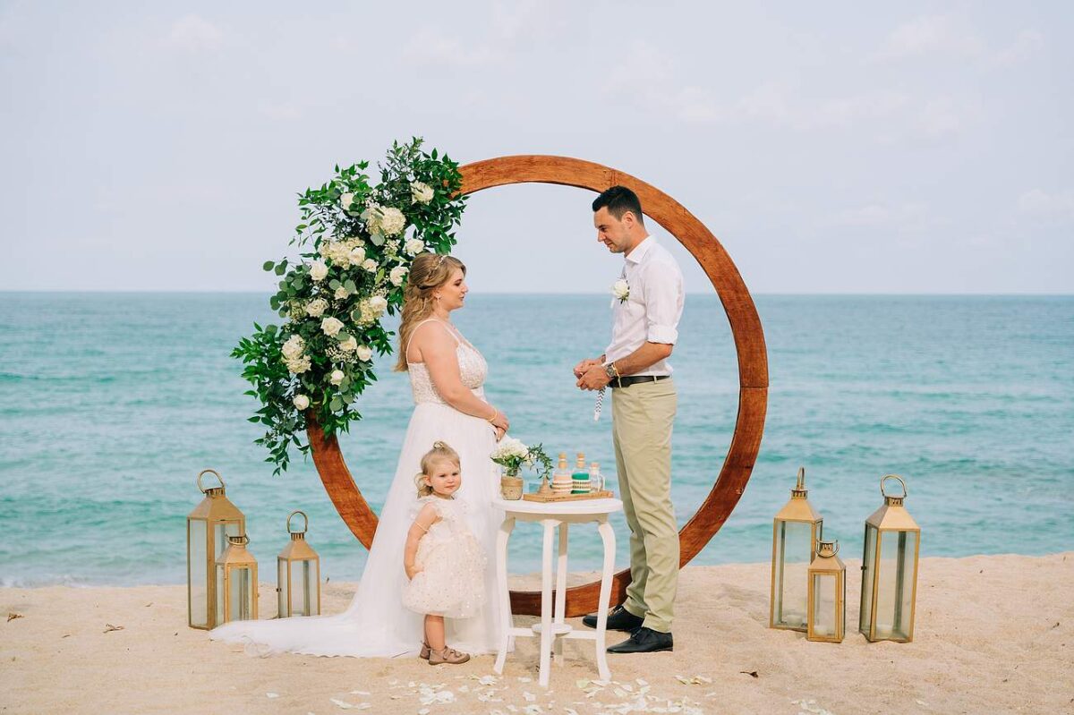 Bride and groom exchanging vows on the beach at New Star Beach Resort, Koh Samui, standing in front of a floral wedding arch.